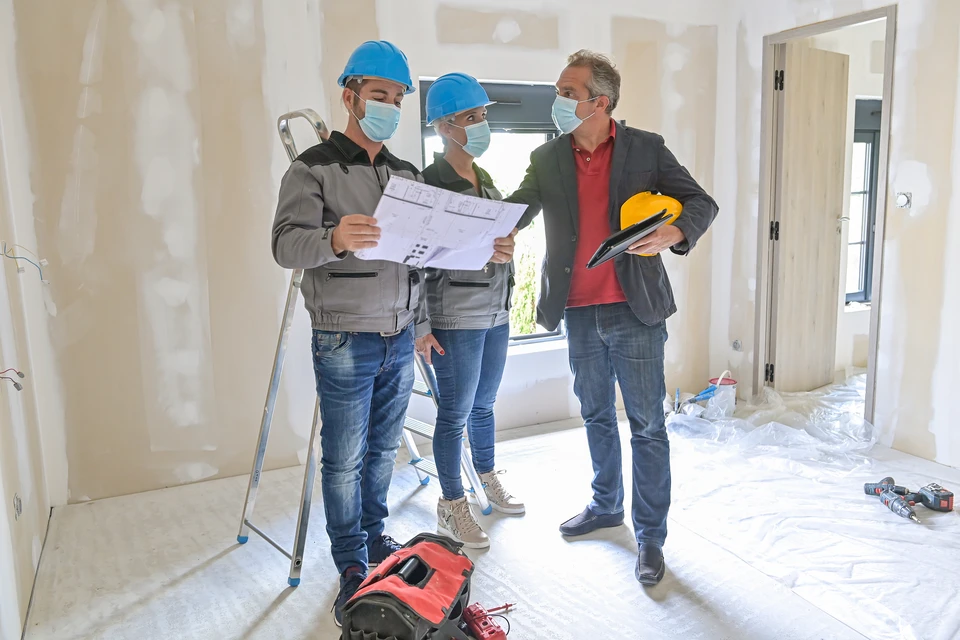 Trois professionnels du bâtiment en réunion de chantier dans un espace en rénovation