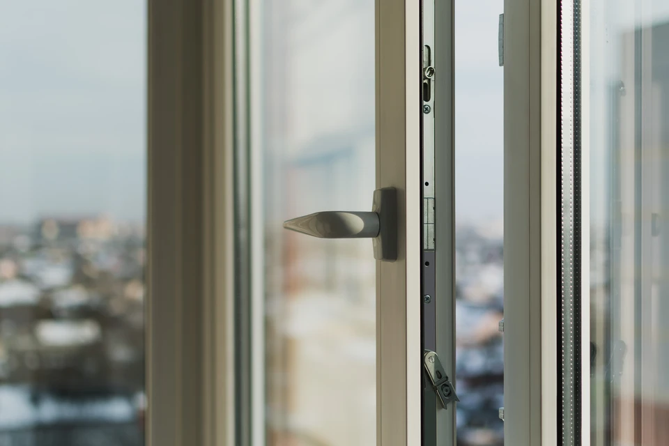 Gros plan d'un artisan en tenue professionnelle effectuant la pose d'une fenêtre isolante en aluminium (menuiserie extérieure) dans le cadre d'une baie vitrée d'une maison en rénovation. L'artisan est concentré sur son travail, manipulant la fenêtre avec ses outils professionnels (équerre, tournevis, etc.). L'arrière-plan montre le cadre de la maison et la lumière naturelle pénétrant par la nouvelle menuiserie. La scène démontre clairement un travail de menuiserie extérieure RGE dans un contexte résidentiel de rénovation.